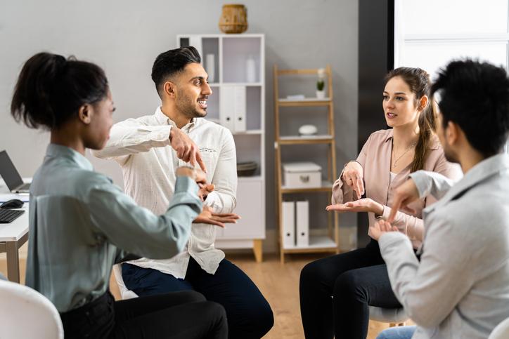 4 young adults sitting in a circle using sign language to communicate
