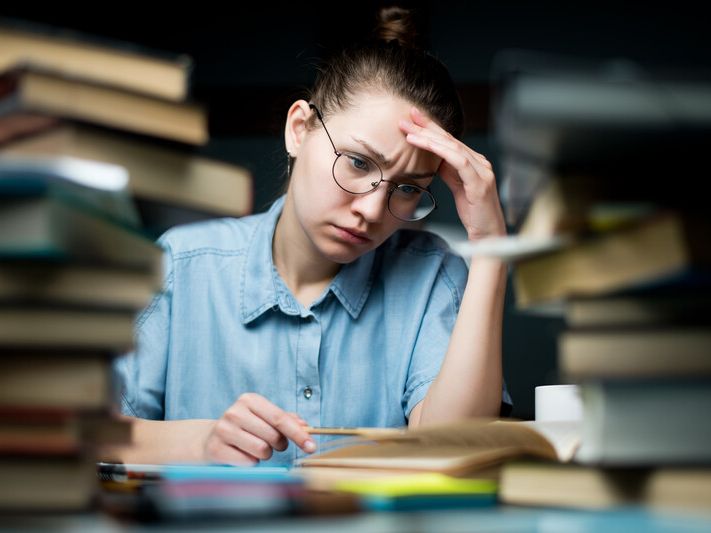 a woman with a frustrated expression studying next to a stack of books