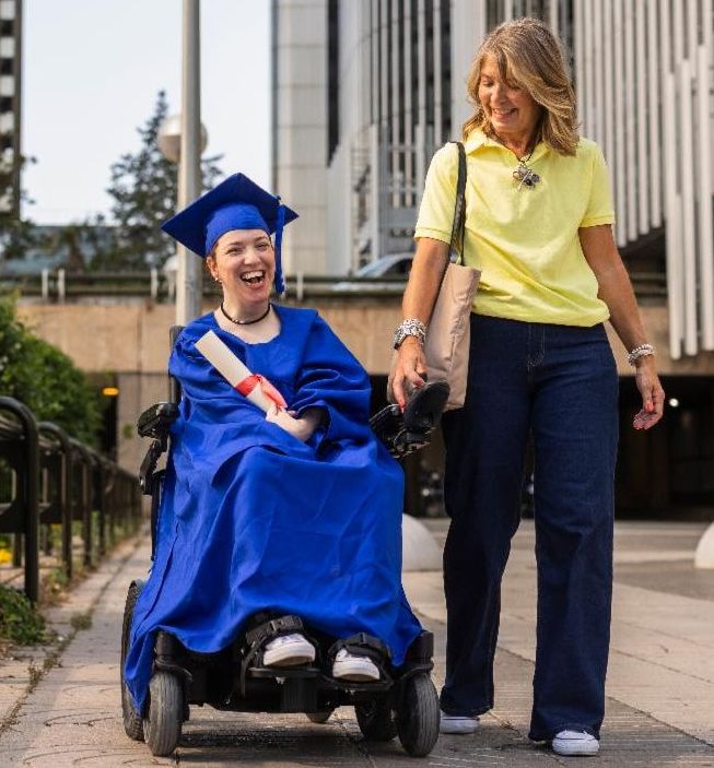 a student in blue graduation gown in wheelchair next to a woman
